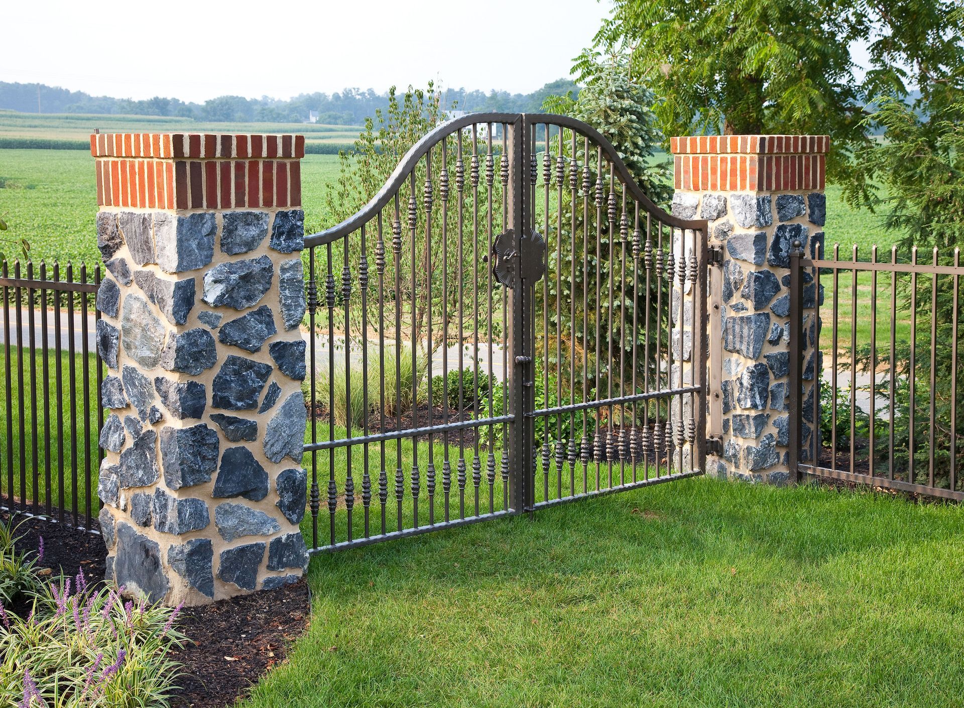 A wrought iron gate is surrounded by stone pillars