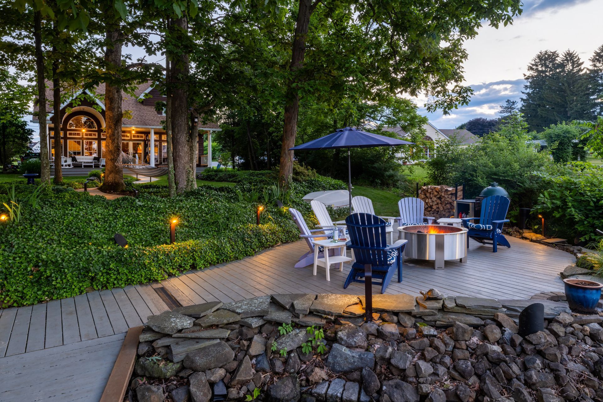 A patio with a fire pit and chairs in front of a house.