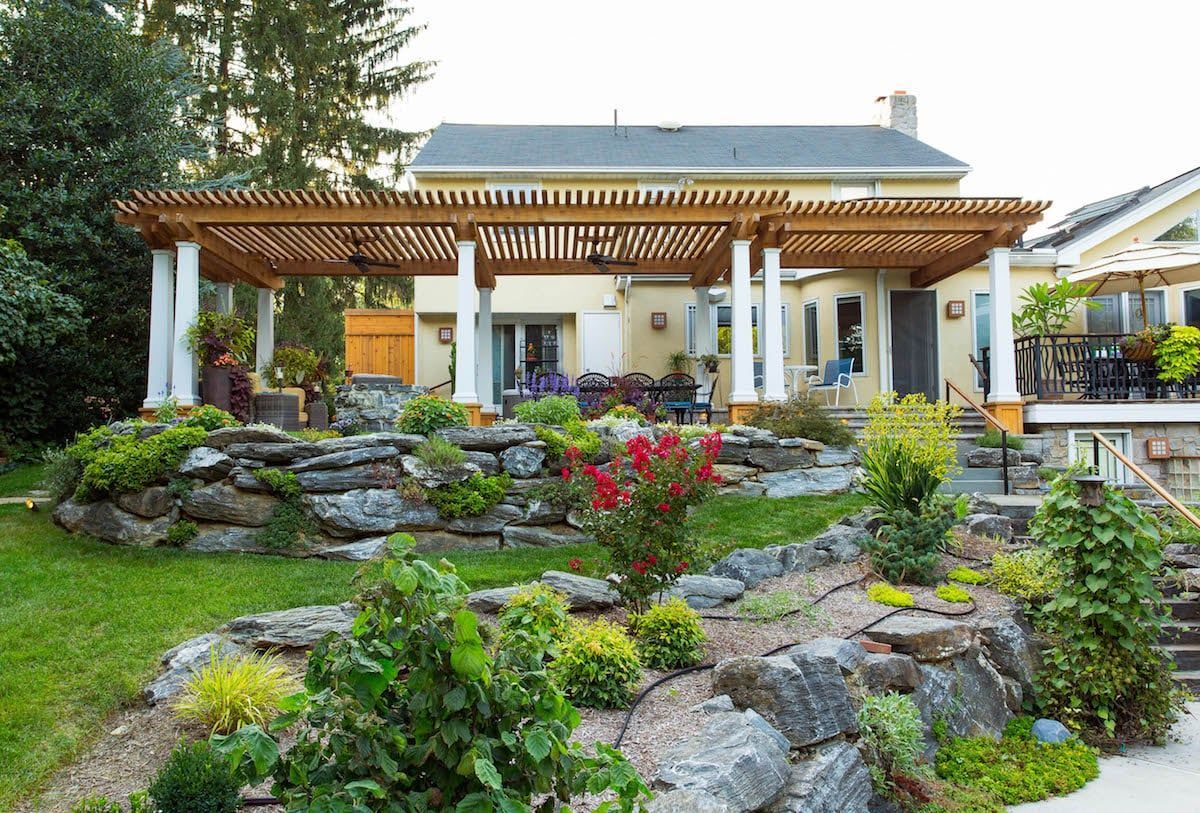 A house with a pergola and a rock garden in front of it.