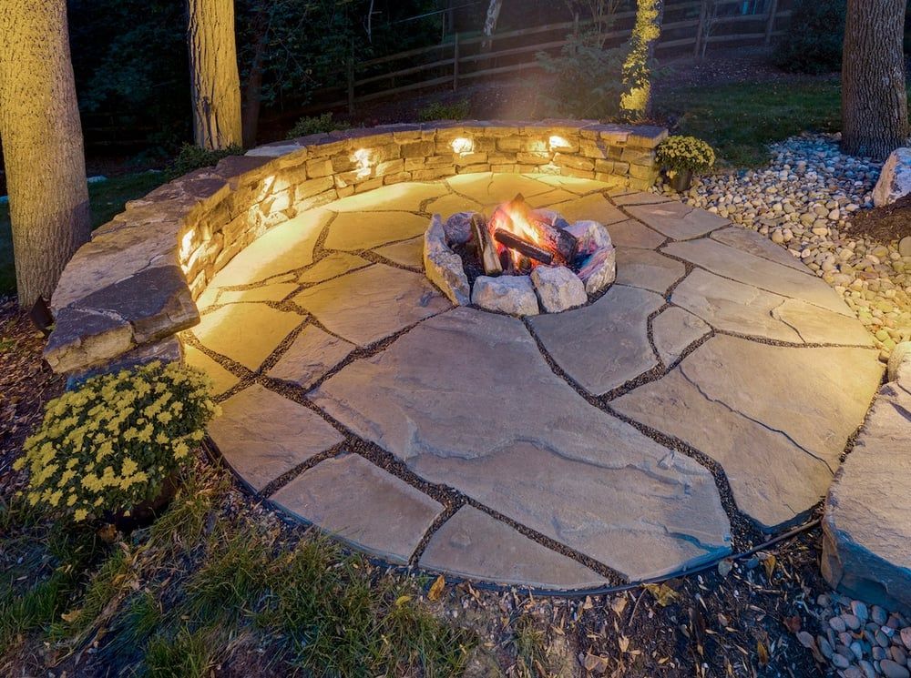 A fire pit in the middle of a stone patio at night.