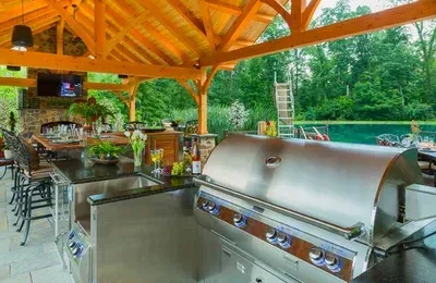 A stainless steel grill is sitting under a wooden roof in an outdoor kitchen.