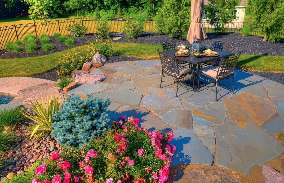 A patio with a table and chairs on it in front of a house.