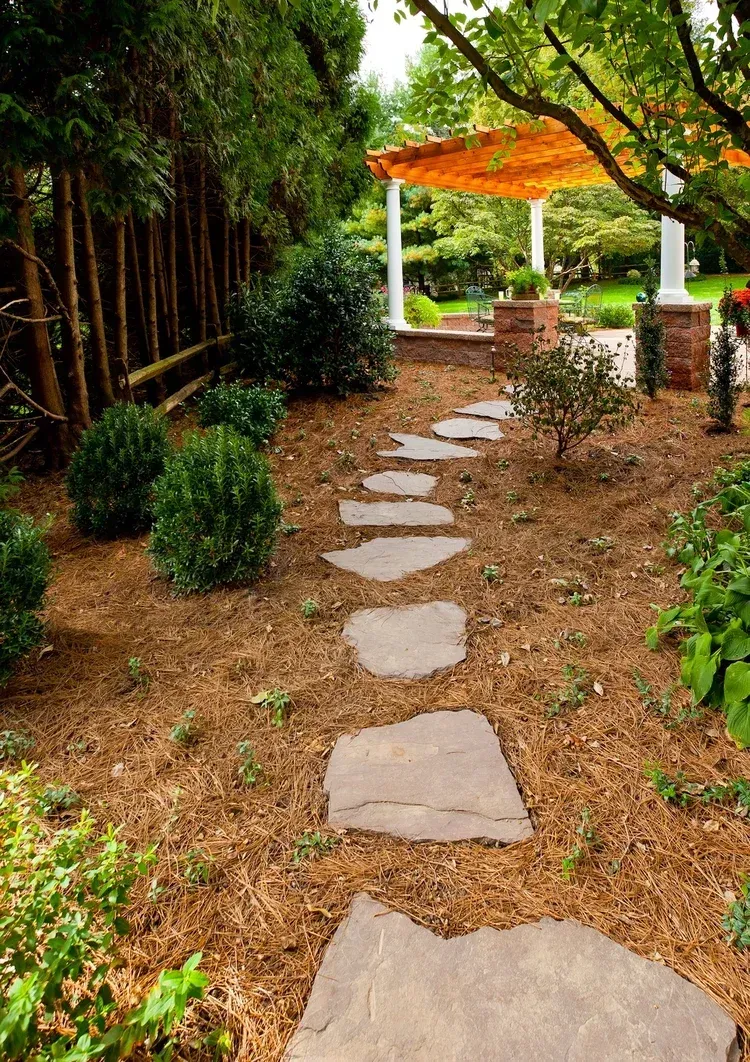 A stone walkway leading to a pergola in a garden.