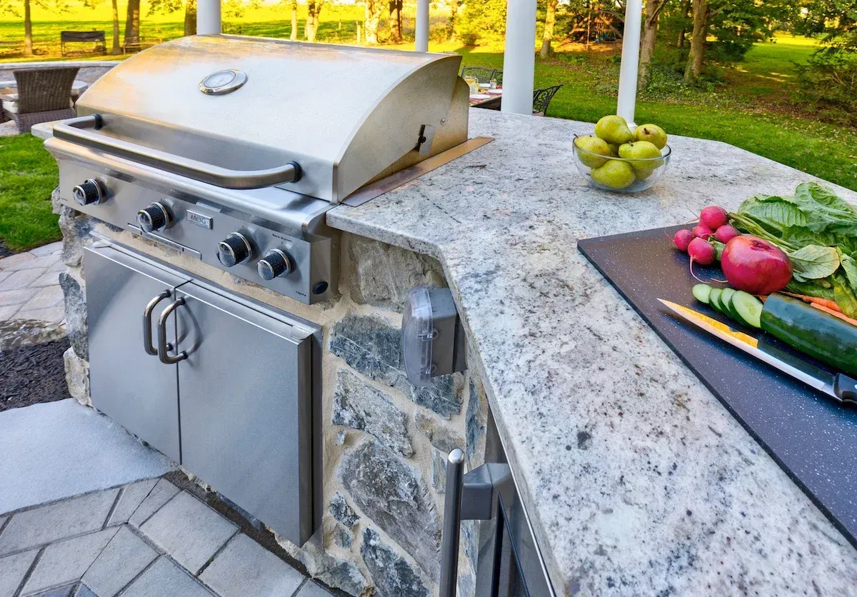 An outdoor kitchen with a grill and vegetables on the counter.