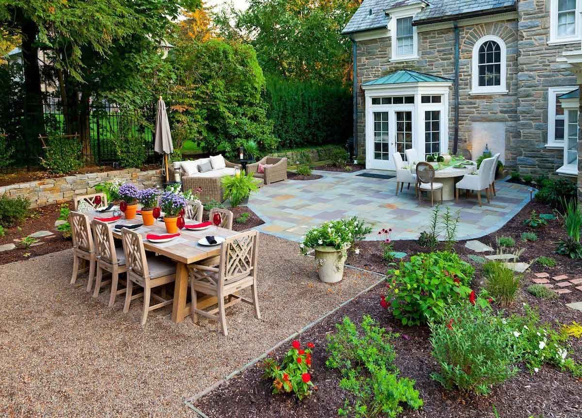 A patio with a table and chairs in front of a stone house.