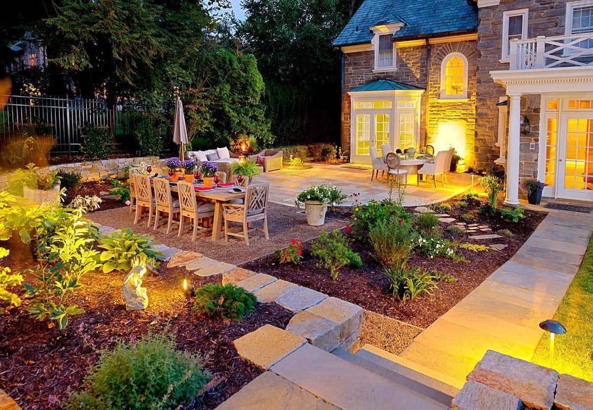 A patio with a table and chairs in front of a house at night.