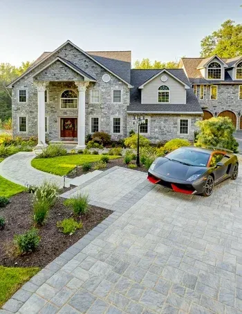 A black sports car is parked in front of a large stone house.