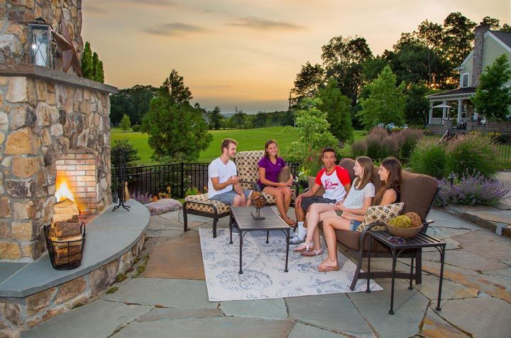 A group of people are sitting around a fireplace on a patio.