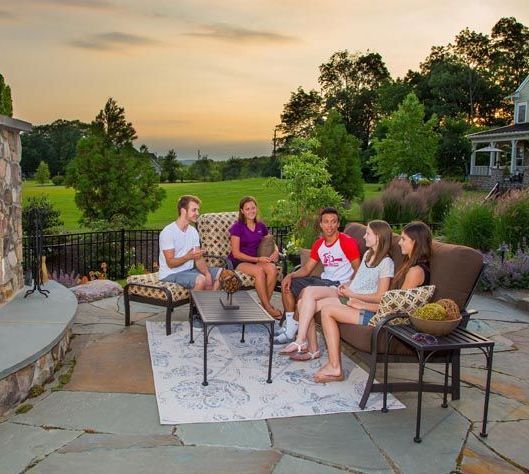 A group of people are sitting around a fireplace on a patio.