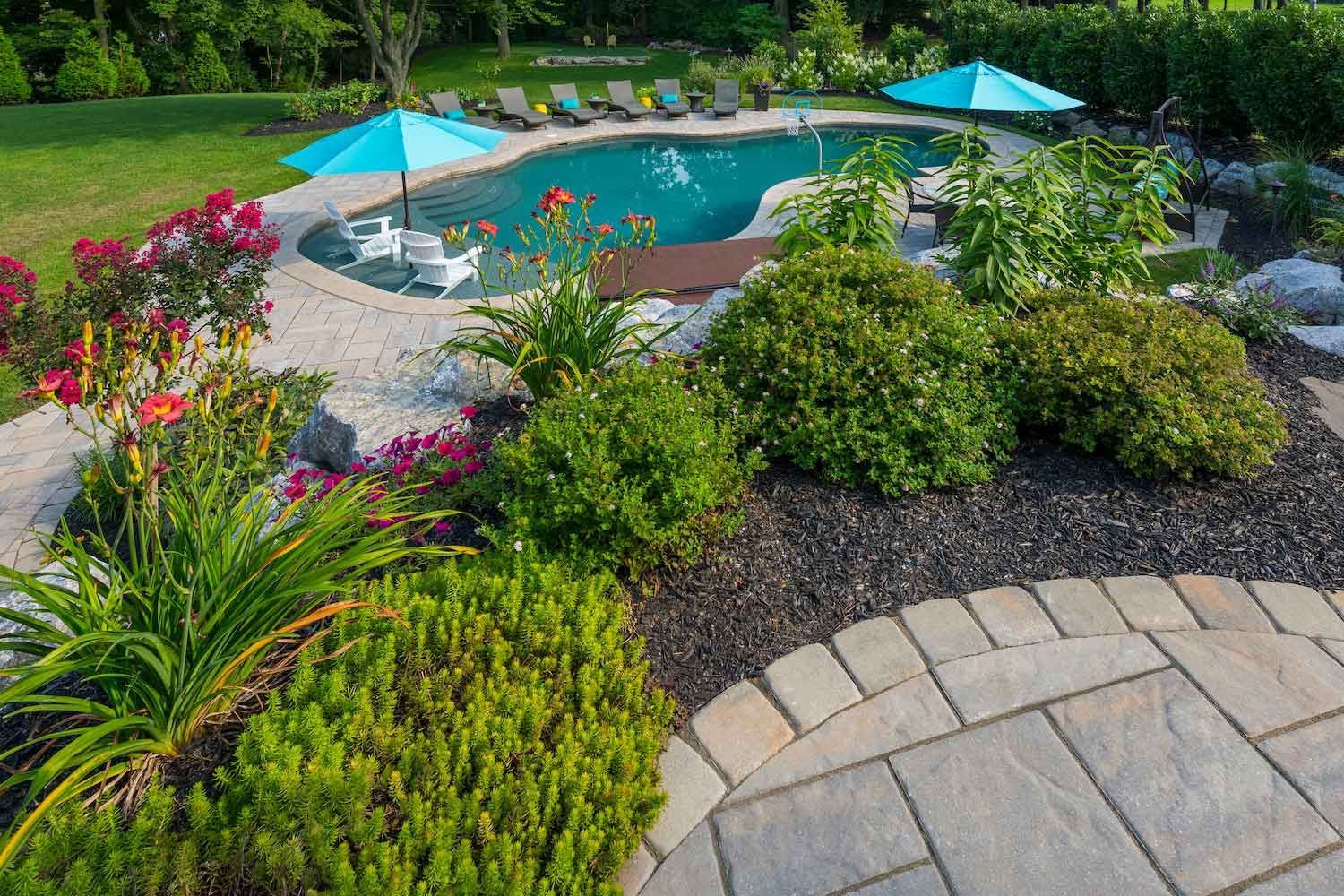 A large swimming pool surrounded by a lush green garden.