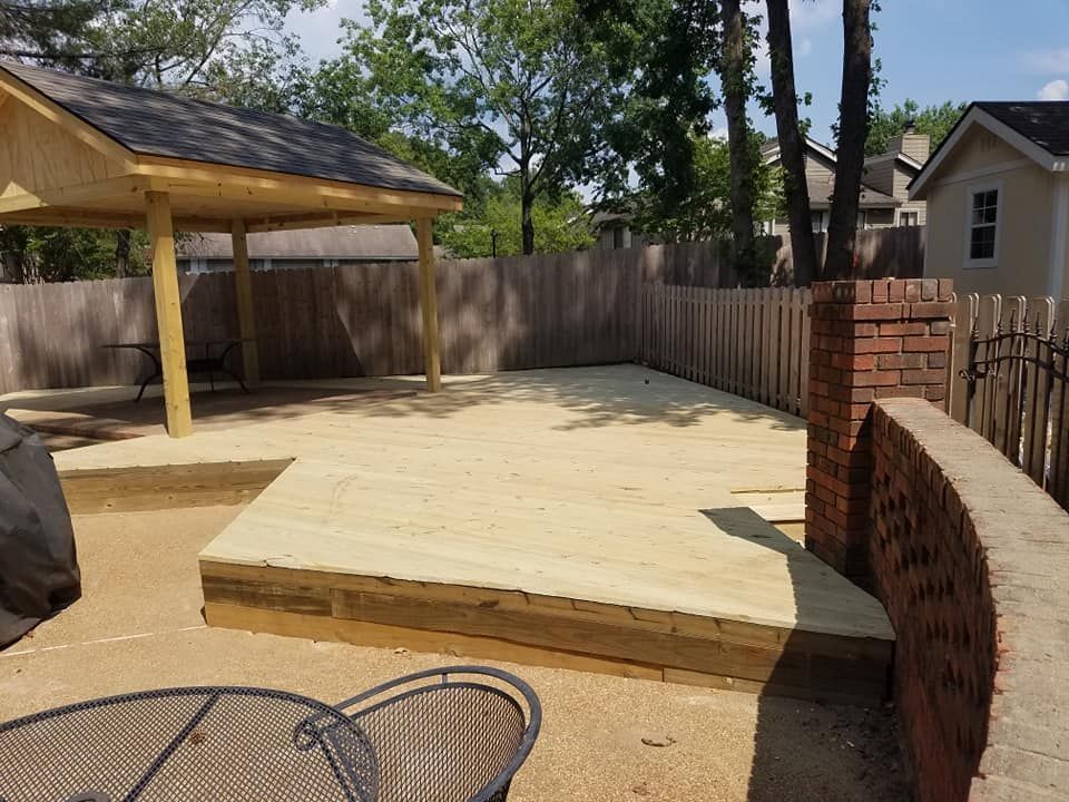 Wooden deck with a covered pavilion in a fenced backyard, sand ground.