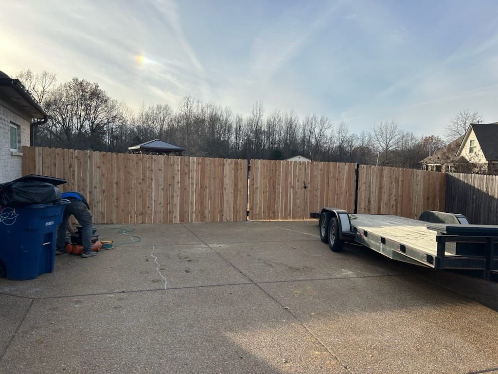 Backyard with new wooden fence and trailer, a person using a saw.