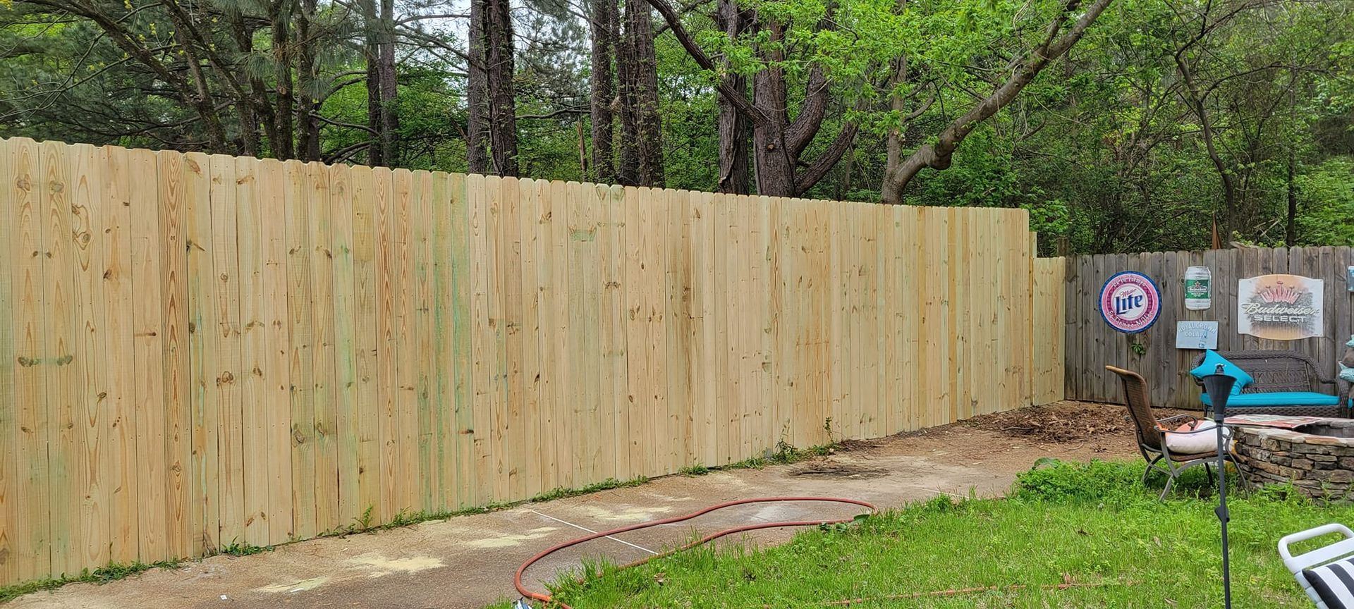 A newly built wooden fence in a backyard with trees in the background.