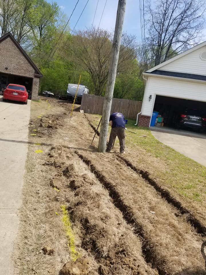 A worker digs trenches along a residential property, near a utility pole.