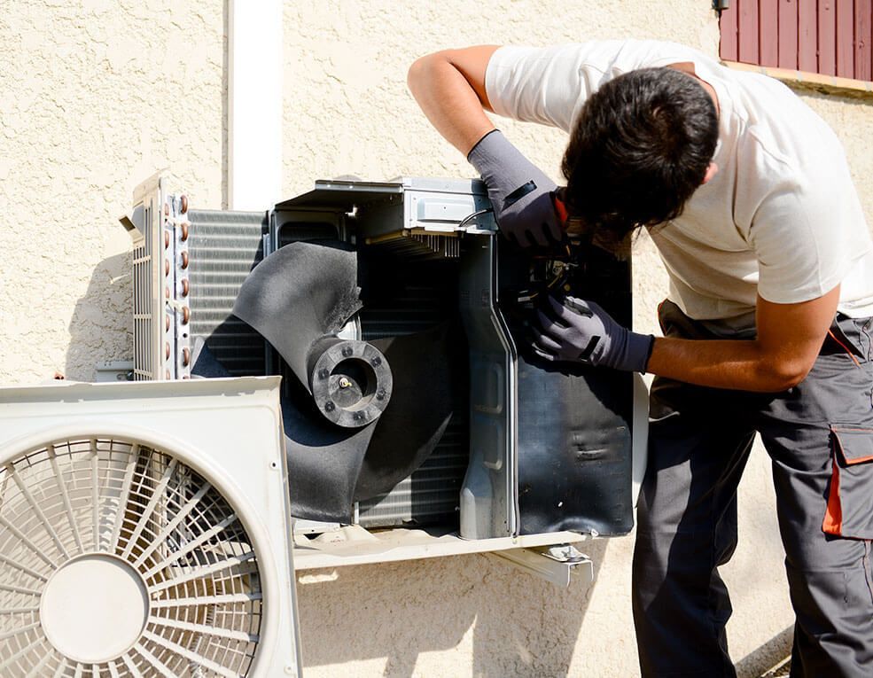 HVAC technician repairing an outdoor air conditioning unit, wearing gloves.