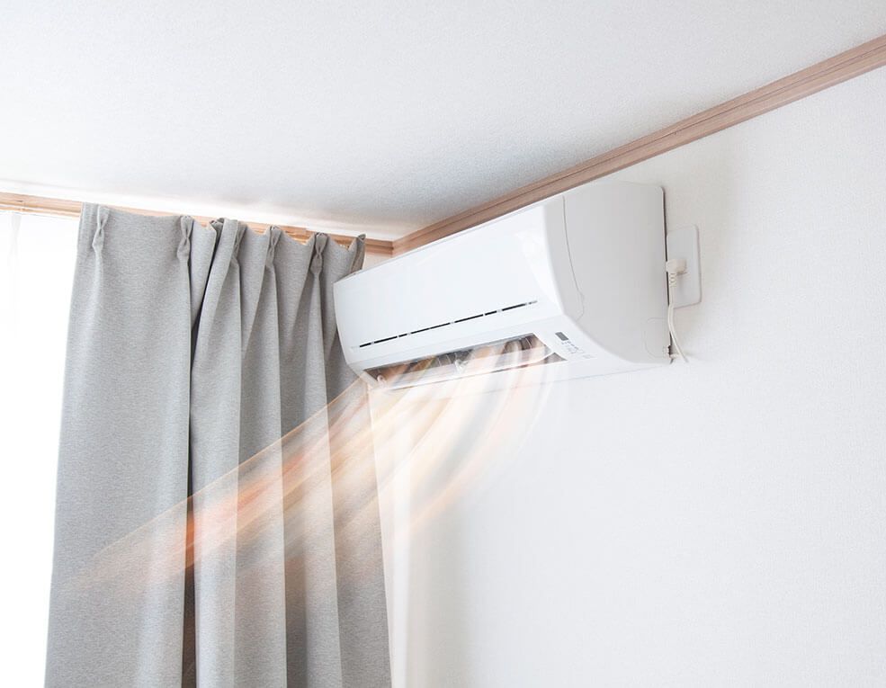 White wall-mounted air conditioner blowing air next to gray curtain.