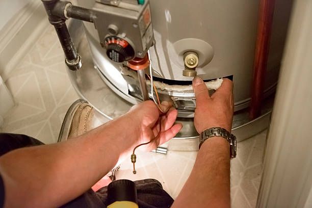 A person's hands working on a gas water heater in a tiled room.