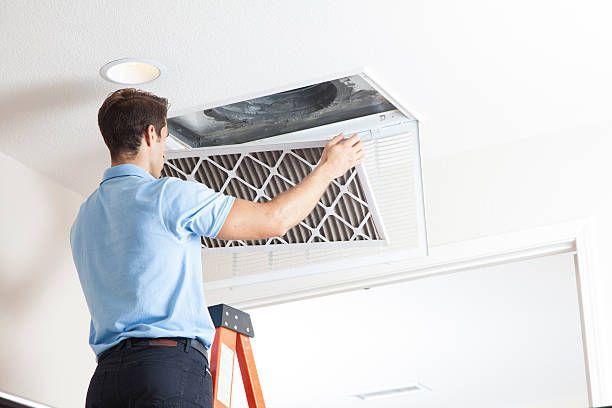 Man replacing an air filter in a ceiling vent. He's on a ladder.