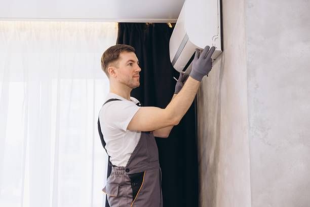 Man in overalls installing an air conditioner on a wall.