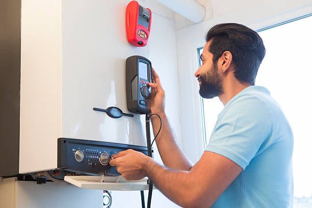 Man adjusts controls on a heating system unit, using a handheld device in a white room.