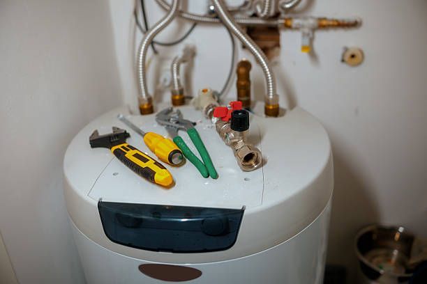 Tools on a water heater: wrench, screwdriver, pliers, and valve components.