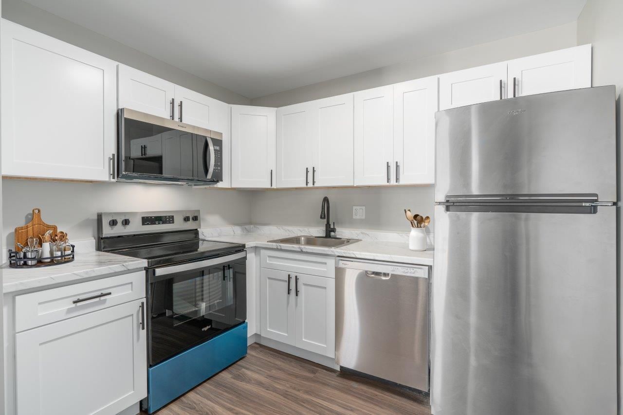 White kitchen with stainless steel refrigerator, stove, microwave, and dishwasher.