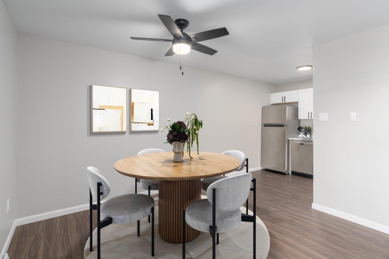 Dining area in an apartment with a round wooden table, six chairs, and a ceiling fan.