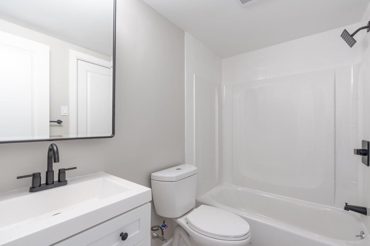 White bathroom with a vanity, toilet, and a tub/shower combo.