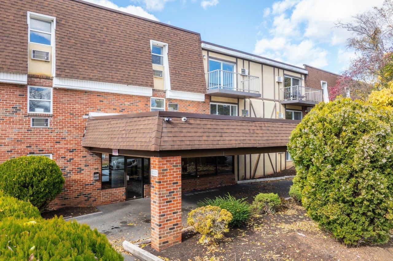 Exterior view of a brick apartment building with a covered entrance and landscaped grounds.