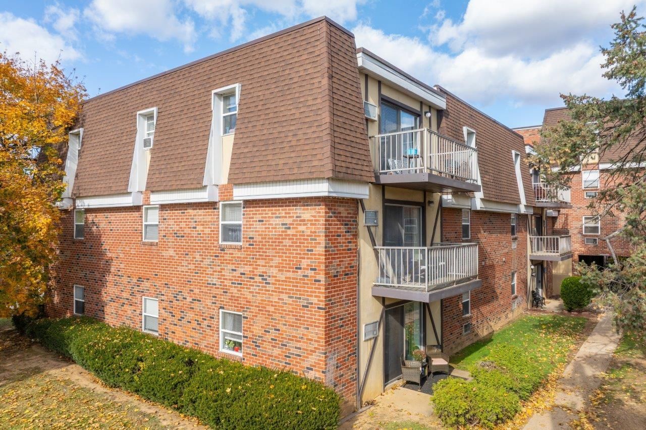 Exterior view of a brick apartment building with multiple balconies and green landscaping.