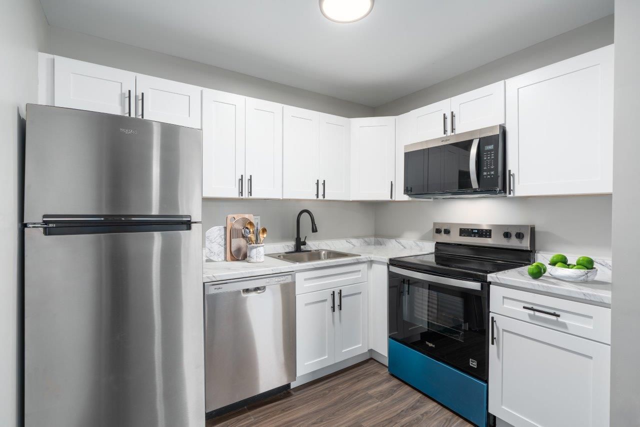 Modern apartment kitchen with white cabinets, stainless steel appliances, and a dark wood floor.