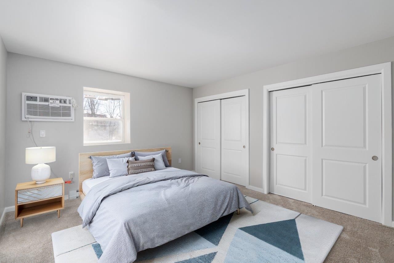 Bedroom in an apartment with a bed, nightstand, window, and double closet doors.
