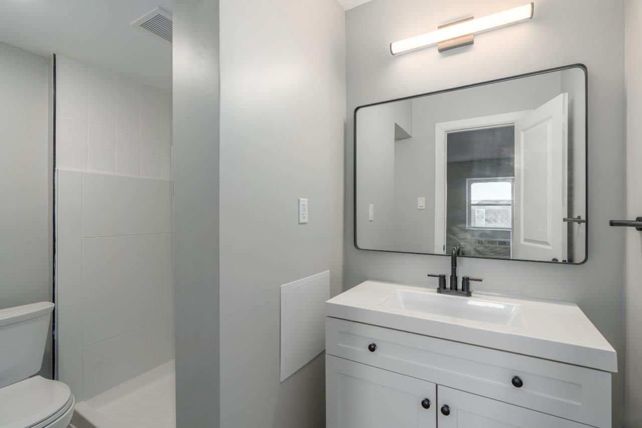 Modern apartment bathroom with white vanity, large mirror, and gray walls.