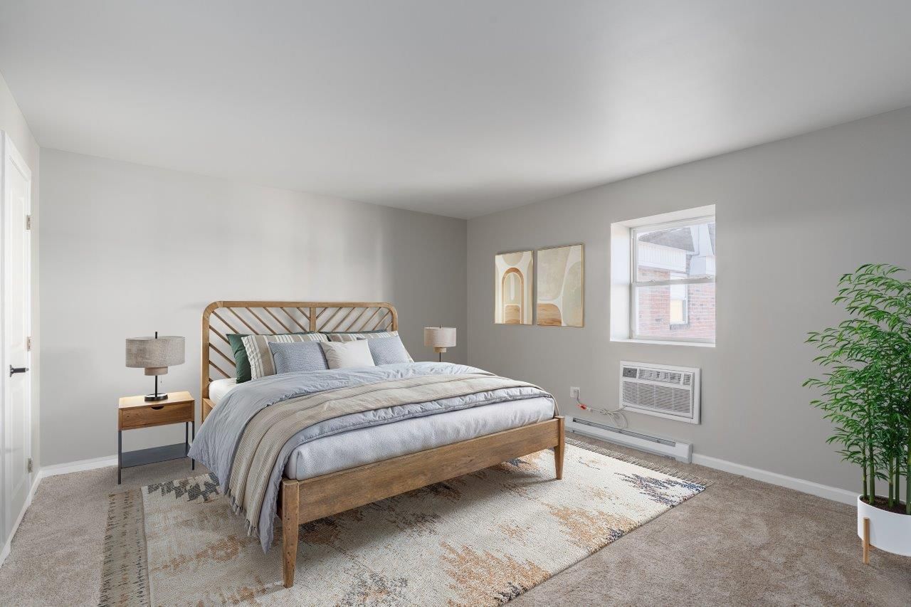 Bedroom in an apartment with a wooden bed, two nightstands, lamps, and a rug.