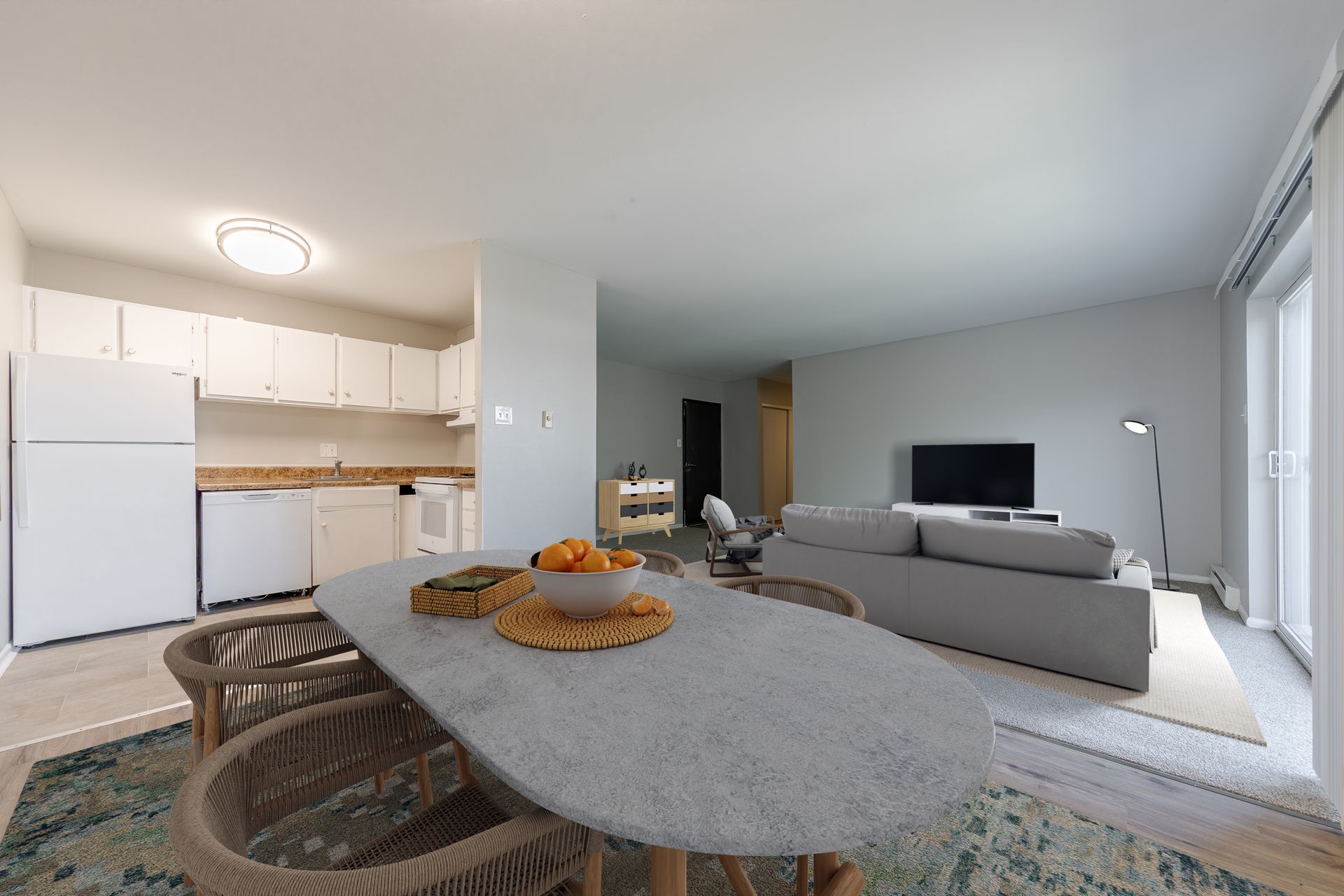 Open-plan living room with gray sofa, TV, dining table, and bright kitchen in the background