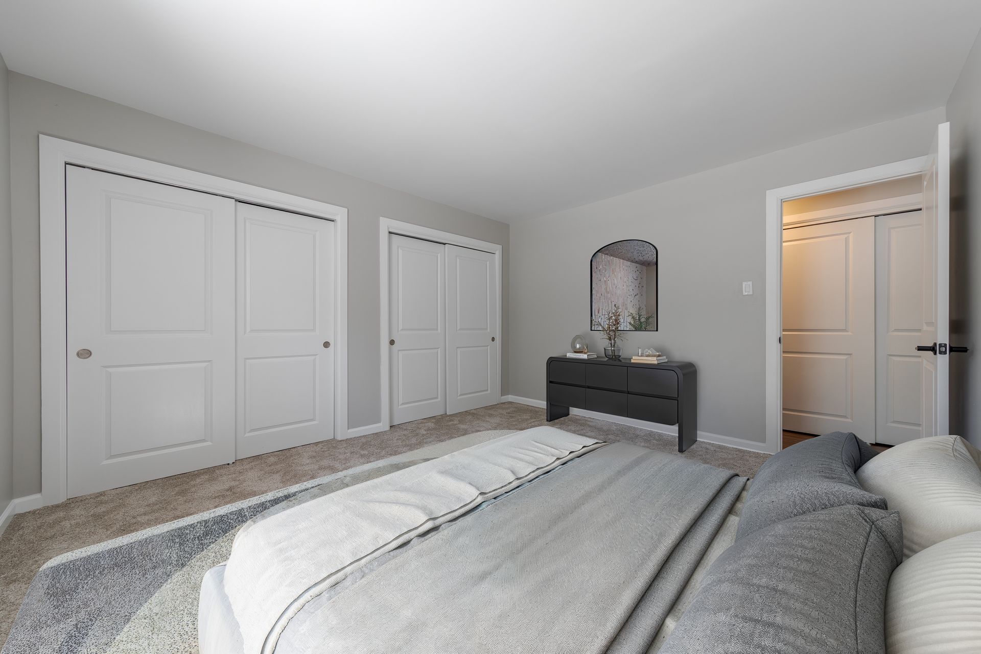 Bright bedroom with a bed, dresser, mirror, and white closet doors in a neutral gray room