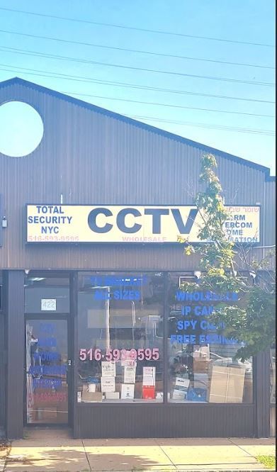 Exterior of a CCTV security store with a sign and window display. Phone number visible, blue tint.