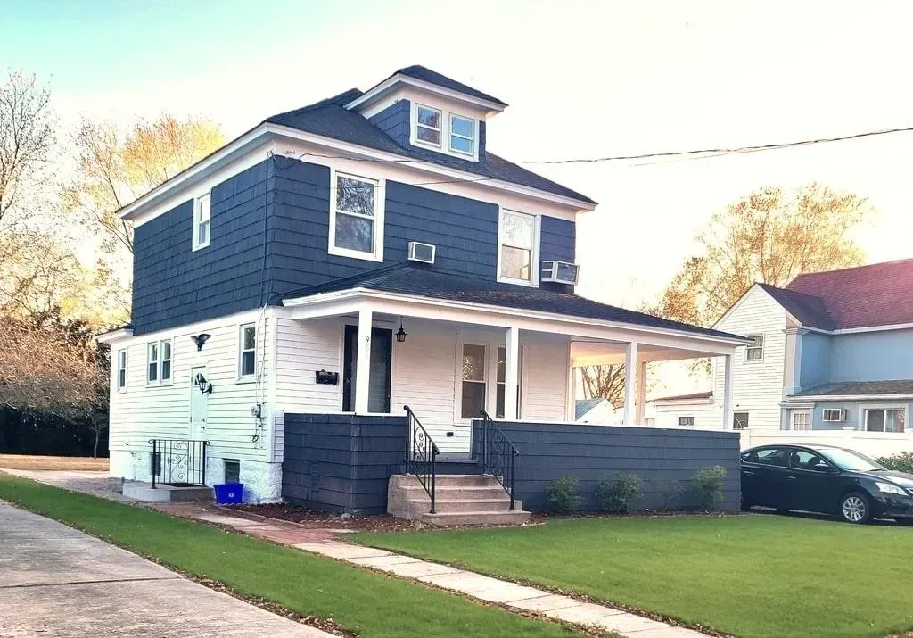 Two-story house with blue siding, white trim, and a covered porch. A car is parked on the right.