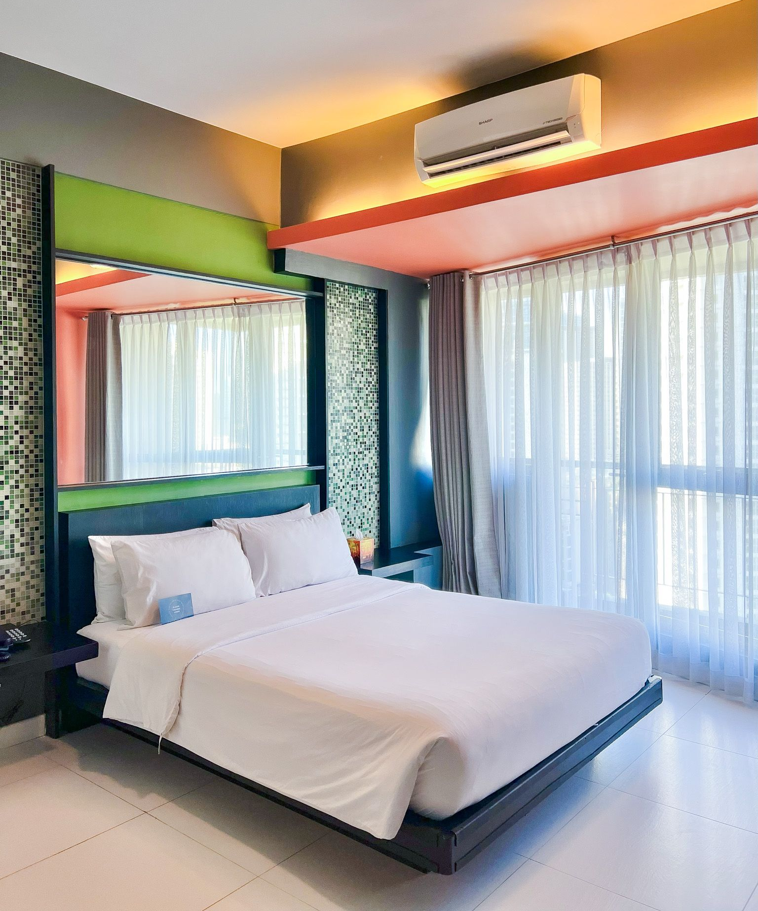 A modern living room with a dark sofa, coffee table, an armchair, tall windows, and three abstract red-toned wall panels.