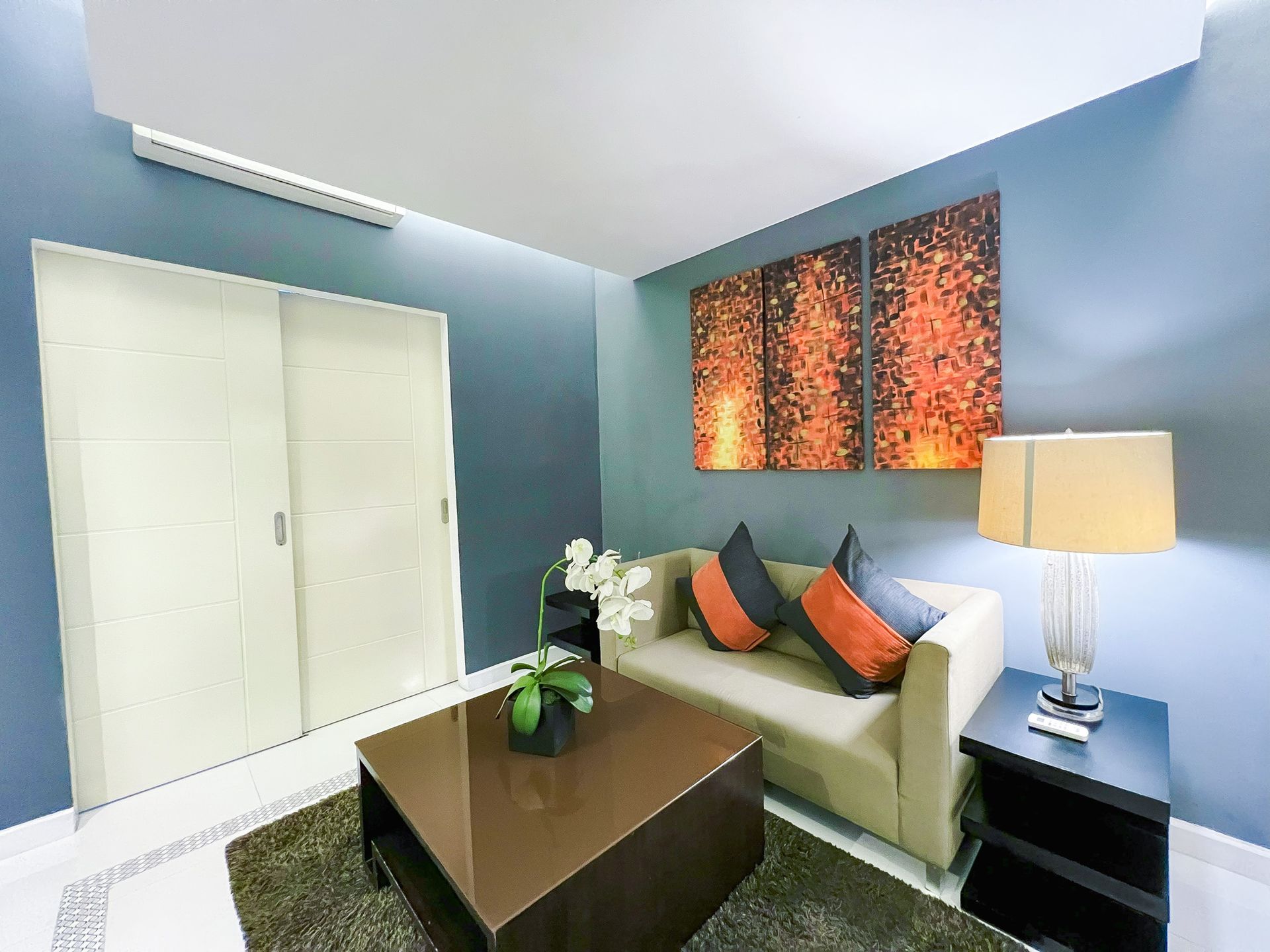 A living room with a beige couch, a brown coffee table, and abstract wall art; blue walls.