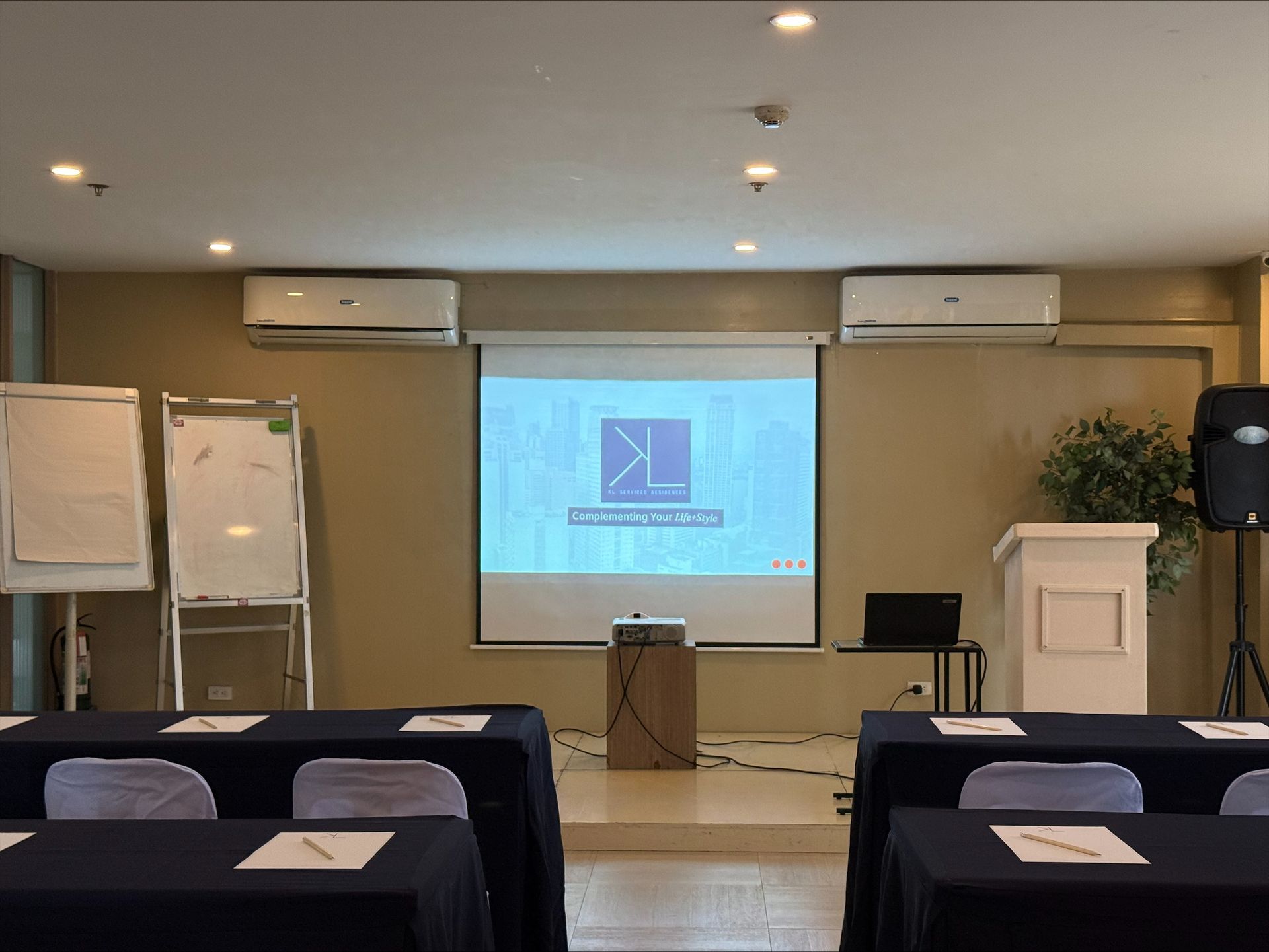 Conference room with tables, chairs, projector screen displaying a logo, and whiteboards.