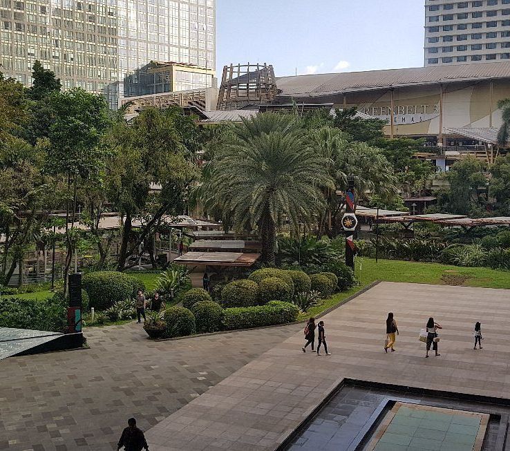 Park with trees and people walking near buildings on a sunny day.