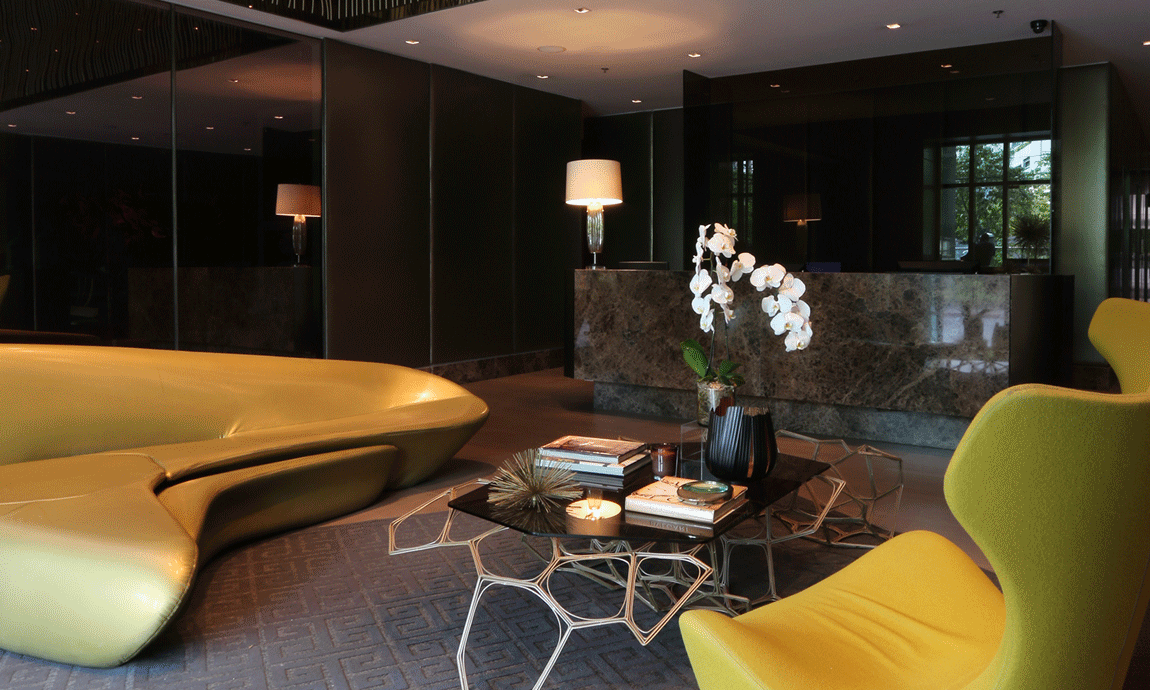 Lobby with gold sofa and yellow chair, marble front desk, and a coffee table with books.