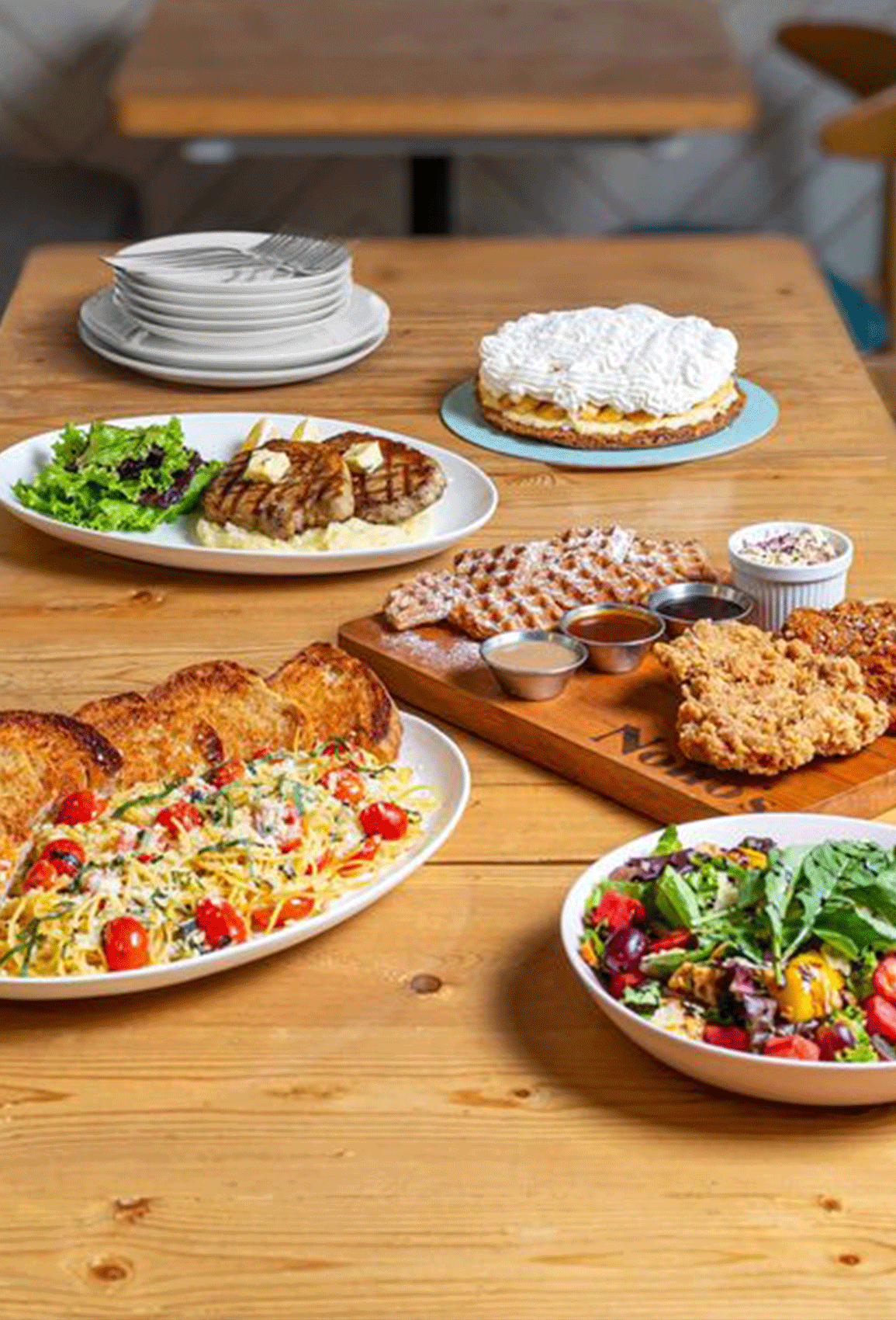 Assorted plated dishes on a wooden table, including salads, pastries, and savory entrées.