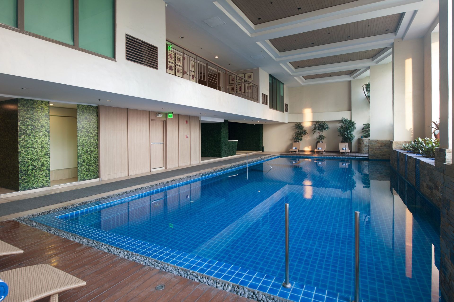 Indoor swimming pool with blue water and tiled floor. Sunlight streams in.