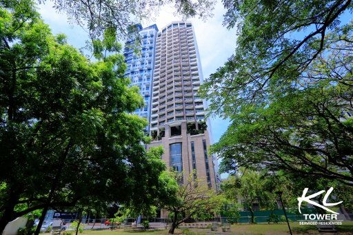 Tall building (KL Tower) framed by green trees against a blue sky.