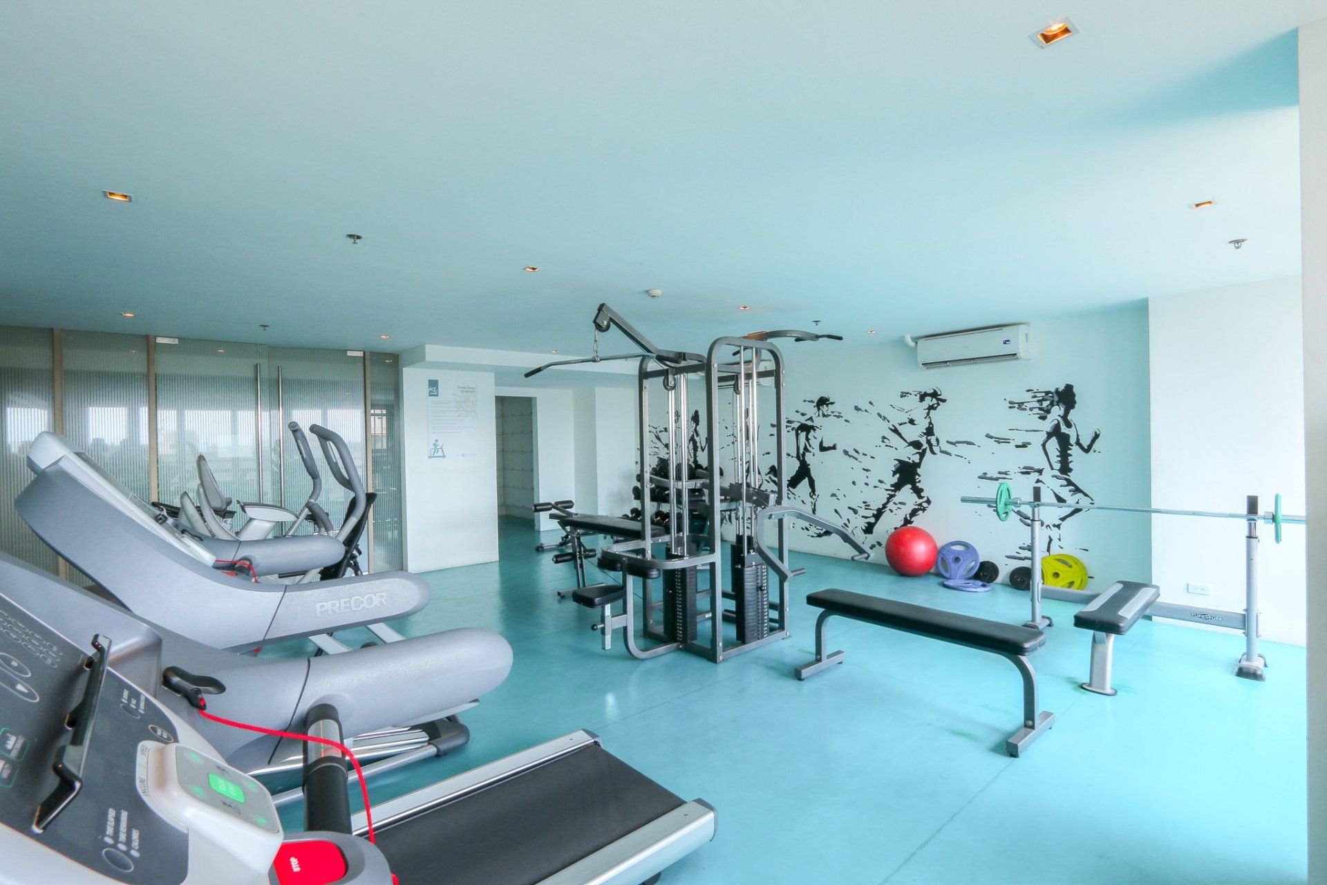 Gym with treadmills, weight machines, bench, and wall art on a light blue floor.