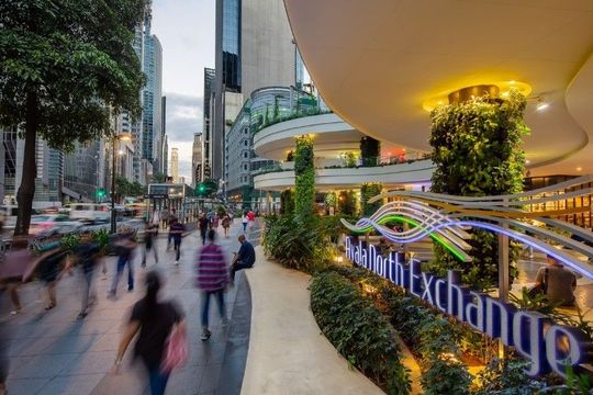 Pedestrians walking near Greenbelt area with shops and landscaped greenery in Makati's commercial district