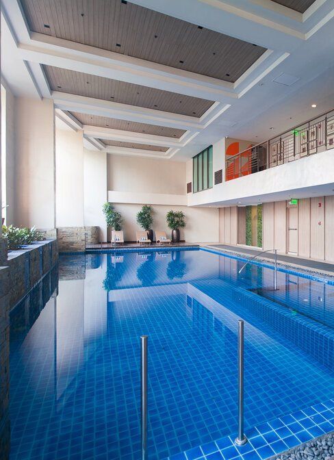 Indoor swimming pool with blue tiled surface, windows, and decorative plants.