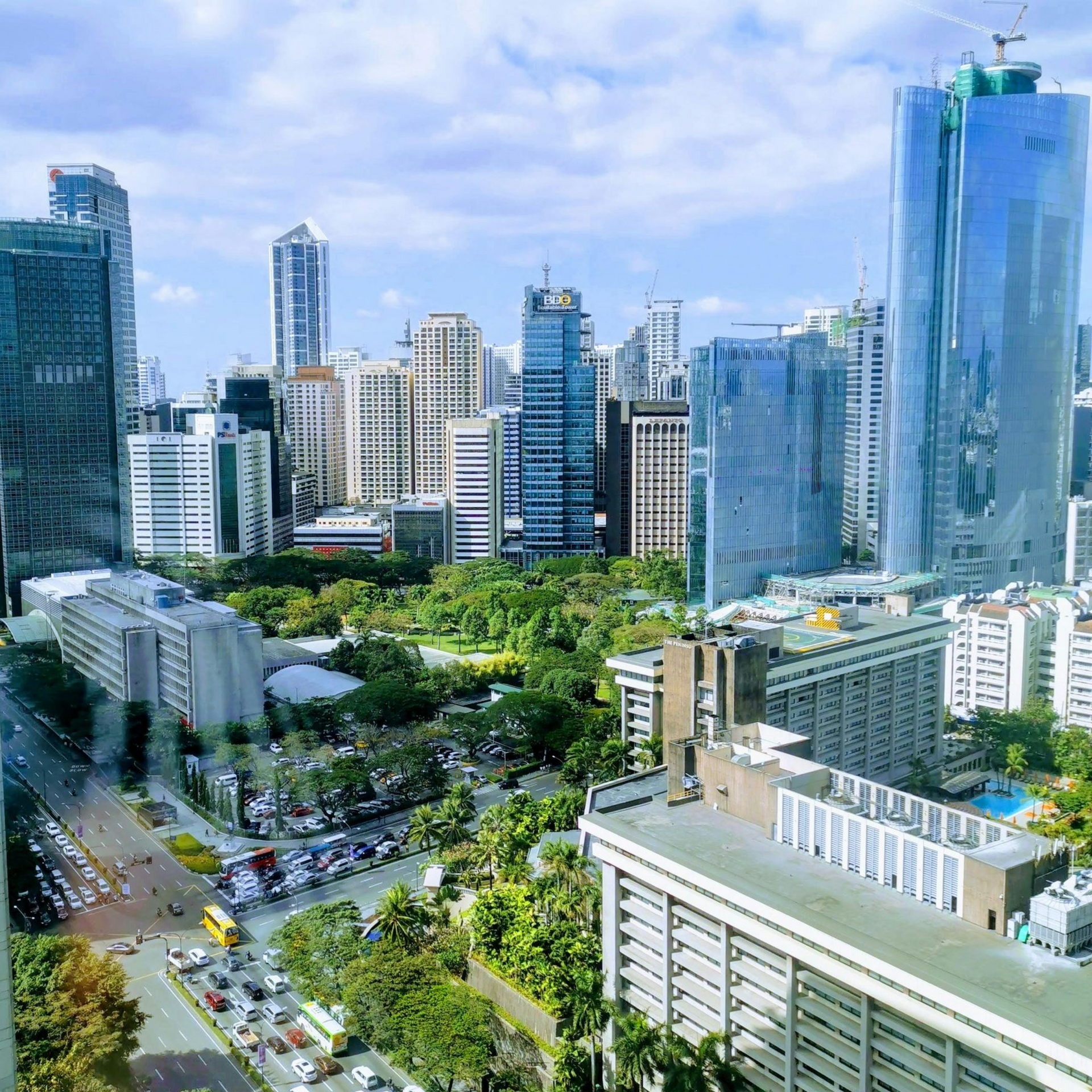 City skyline with tall buildings, green trees, and a blue sky.
